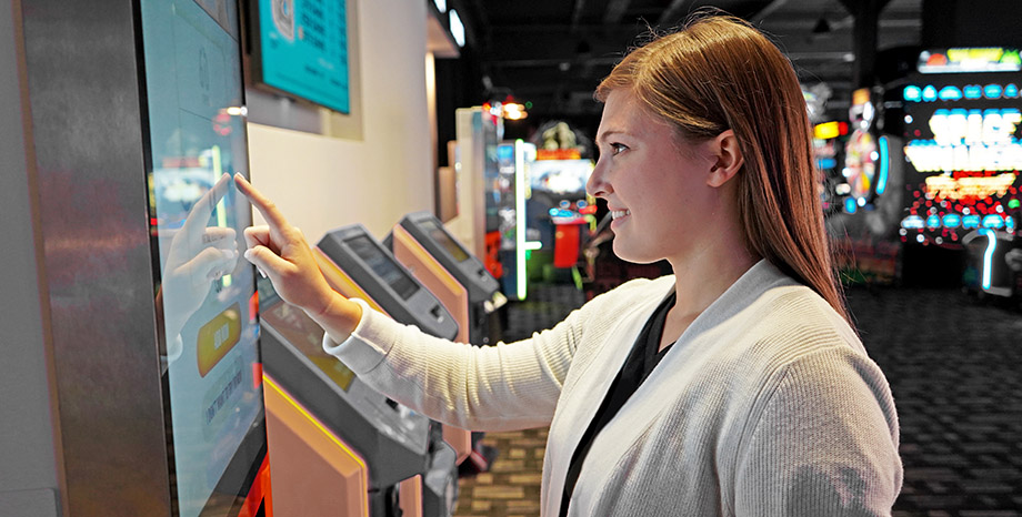 A woman smiles as she interacts with a touchscreen to represent self-service retail solutions