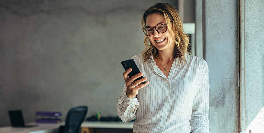 Woman smiles while looking at her smartphone to represent Vynamic Self-Service Enterprise Manager