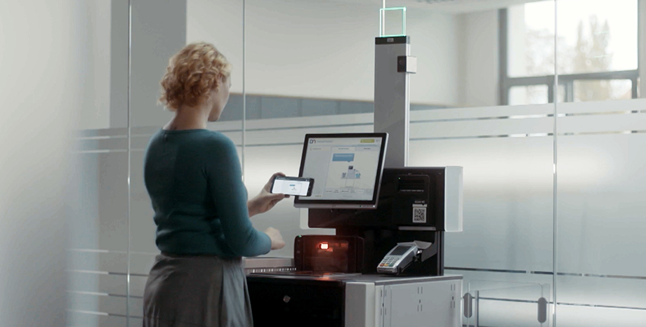 Over the shoulder view of a woman checking out at a store self-service kiosk using her smartphone