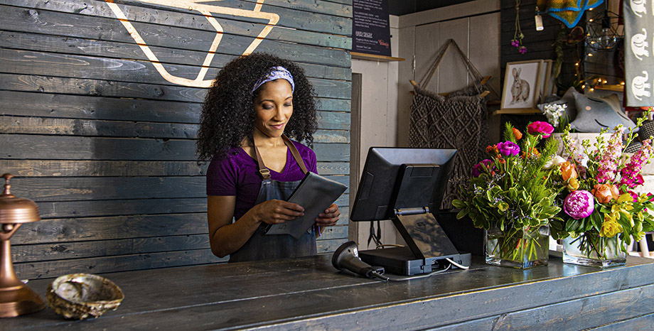 Female business owner stands behind the counter of her flower shop looking at a retail POS system monitor