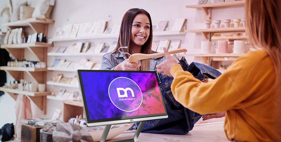 Woman hands clothes to a sales clerk for checkout, next to computer monitor with DN Series BEETLE retail POS systems logo